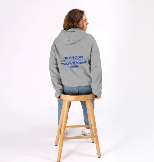 Oversized organic cotton hoodie with 'Be proud of how far you've come' laid flat. Showcasing the relaxed fit and inspiring message. Sustainable and stylish streetwear for self-improvement.